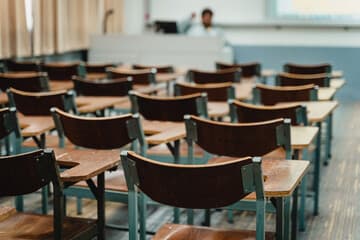 An empty classroom with rows of unused desks in soft natural light.