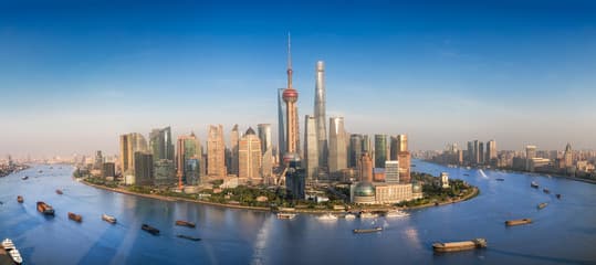 The Shanghai skyline at dusk with idle construction cranes and glowing financial-district lights.