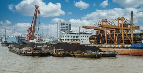 A rare earth mineral processing facility with ore piles and stacked shipping containers.