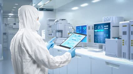 Technicians in protective suits inside a blue-lit semiconductor cleanroom.