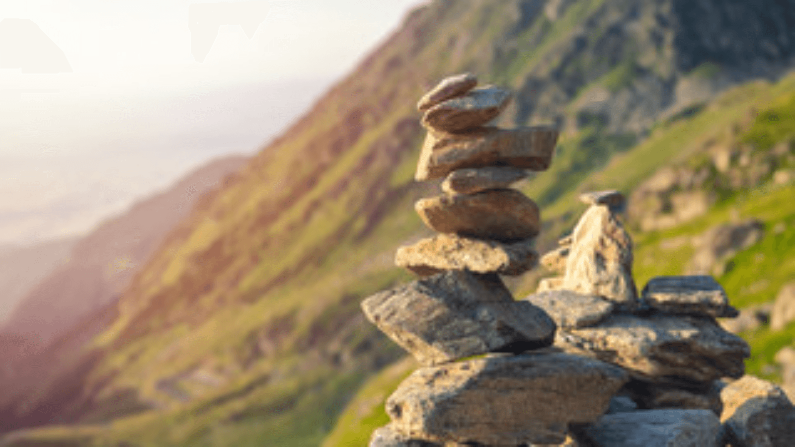 A balanced stack of stones on a mountainside overlooking a valley at golden hour
