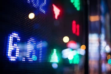 A trading floor with red and green digital tickers and oil barrels in shadow, symbolizing mixed global growth.