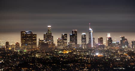 A Middle Eastern port city skyline at night with distant light trails in the sky