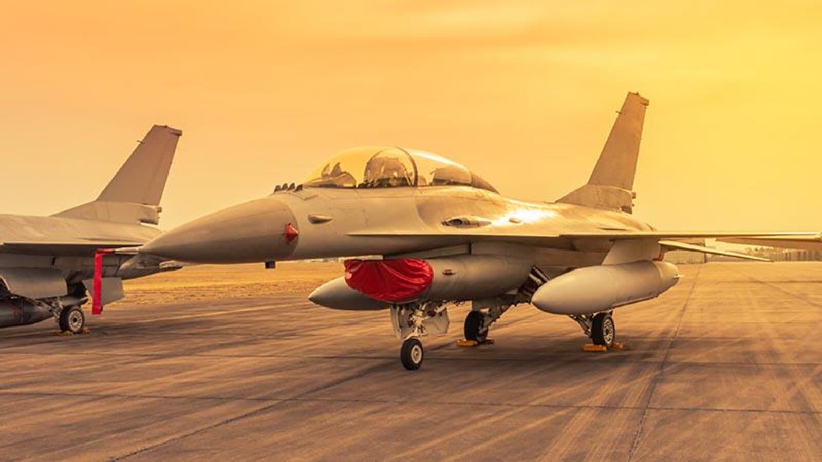 A fighter jet parked on a military airbase tarmac under an orange sunset sky