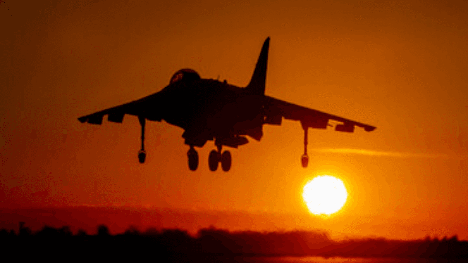 A military jet in silhouette taking off against a fiery orange sunset