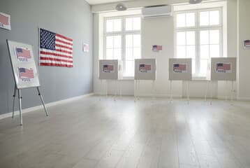An empty polling place with blurred campaign signage and an American flag.