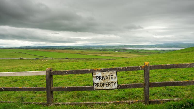 An empty rural border landscape with a damaged fence line and faint smoke on the horizon