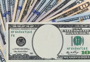 A stack of hundred-dollar bills beside a rising debt chart, financial district blurred behind.
