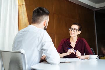 Two backlit silhouettes facing each other across a table in conversation.